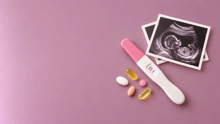 Positive pregnancy test beside overlapping baby ultrasound prints and a few prenatal supplements on a dusty mauve background.