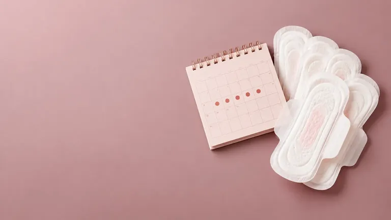 White menstrual pads beside a baby-pink calendar with period days marked, arranged on a clean dusty-mauve background.